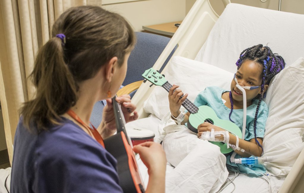 cropped photo Young girl in hospital bed plays the ukulele with a Teaching Artist during a music workshop